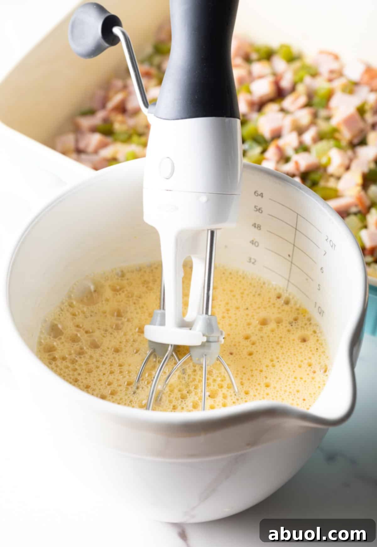 An egg and cream mixture is being whisked together in a white measuring bowl.