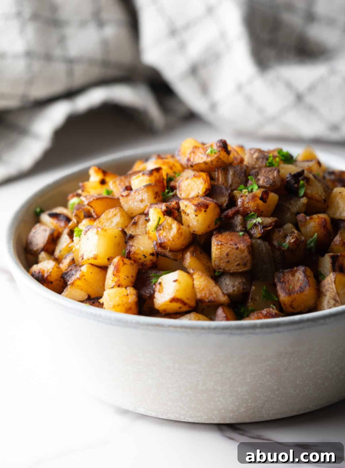 Golden Pan Fried Potatoes 10 A side profile view of a white bowl overflowing with golden, crispy homemade skillet potatoes.