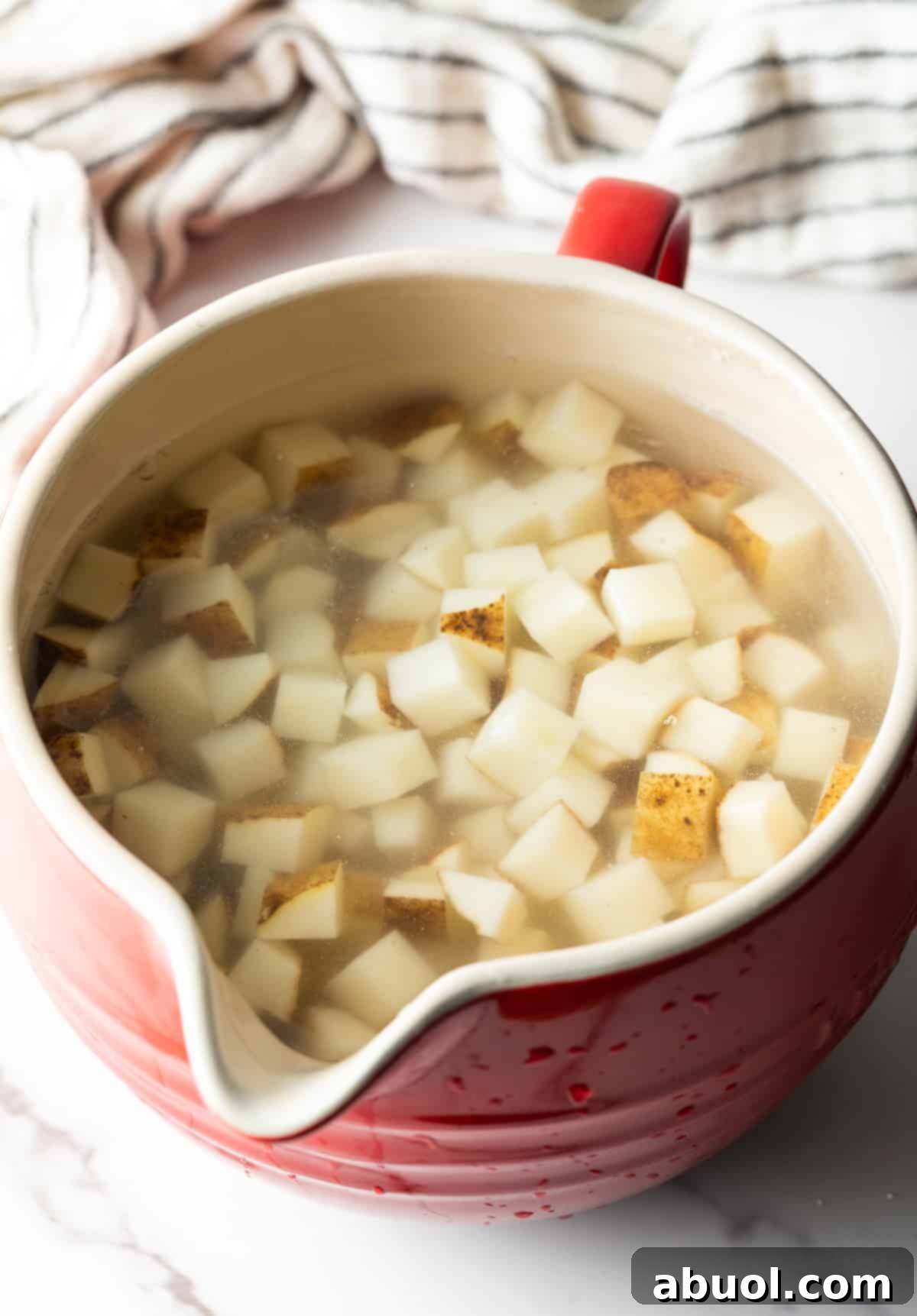 Golden Pan Fried Potatoes 5 Cubed russet potatoes soaking in a red bowl filled with ice water to remove starch.