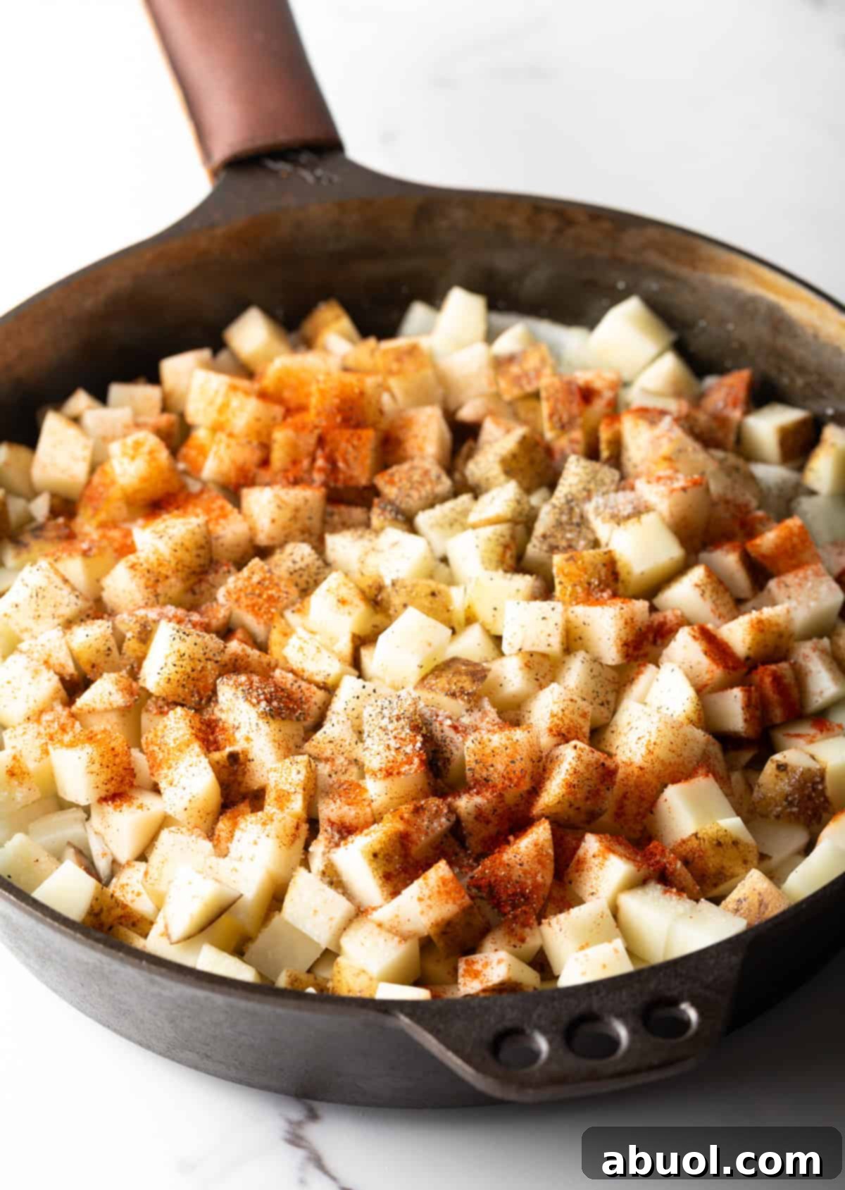 Golden Pan Fried Potatoes 6 Raw, seasoned potato cubes in a black skillet before cooking, sprinkled with smoked paprika.