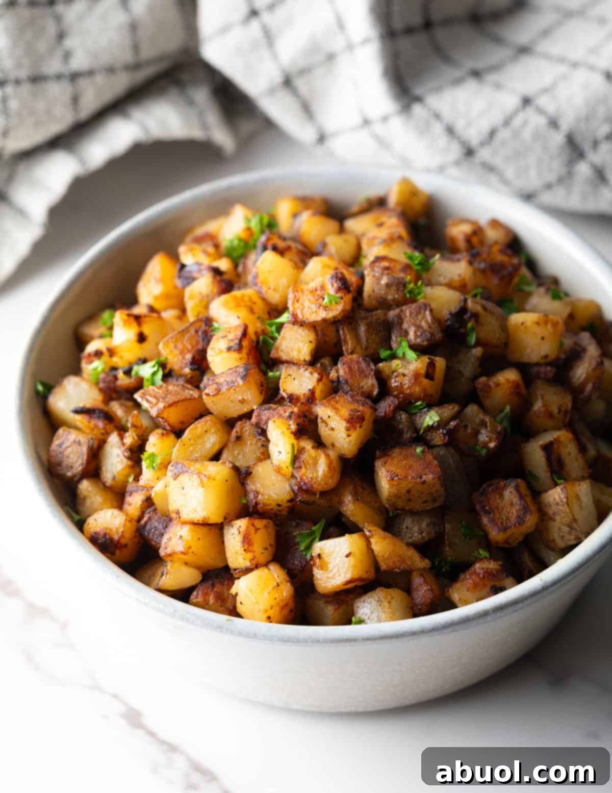 Golden Pan Fried Potatoes 9 Crispy homefries in a white serving bowl, topped with fresh parsley.