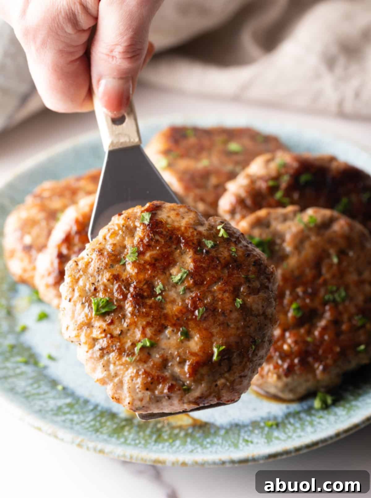 A metal spatula lifting a perfectly browned homemade breakfast sausage patty from a plate.