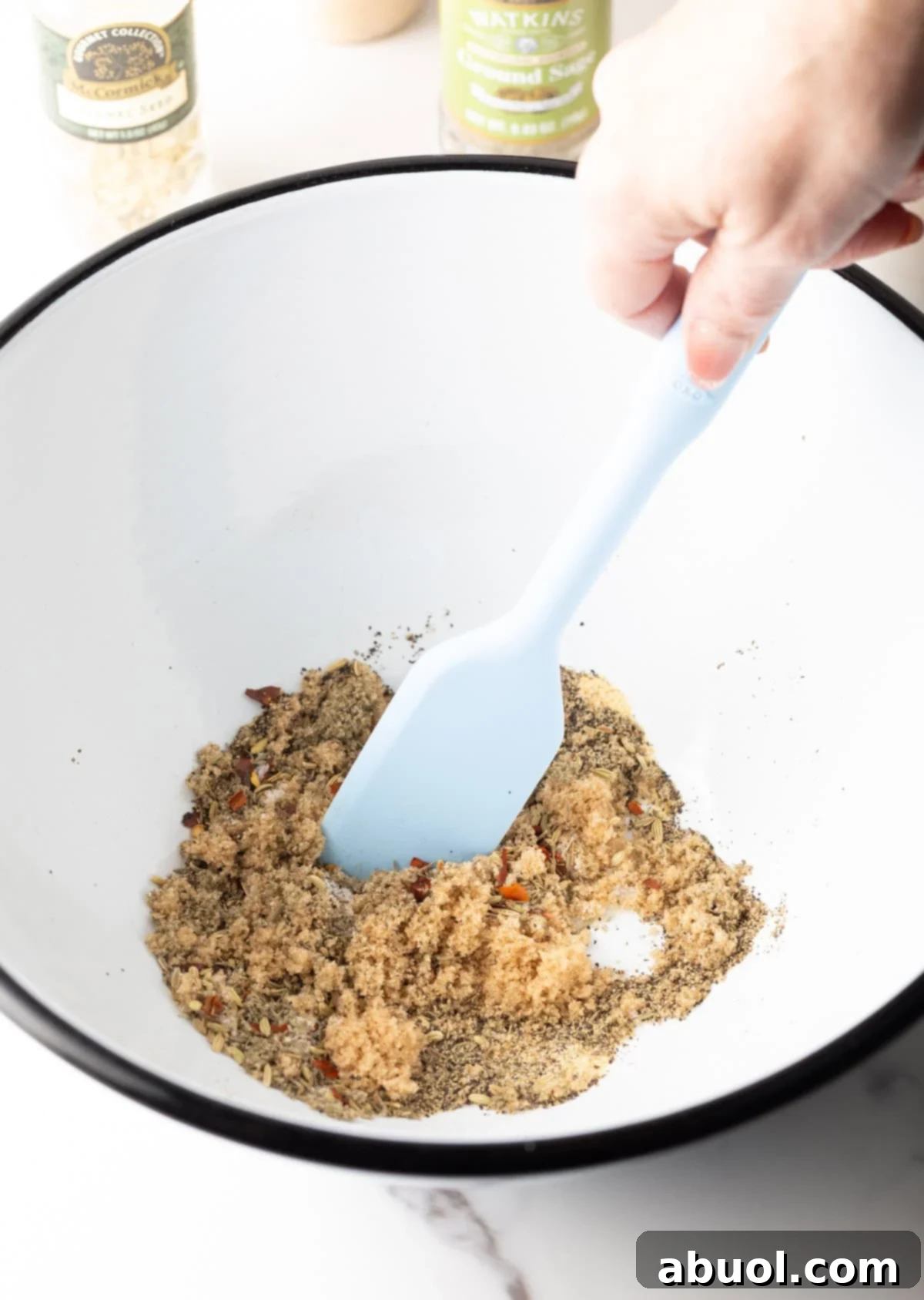 A spatula stirring together a blend of herbs and spices for breakfast sausage in a white bowl.