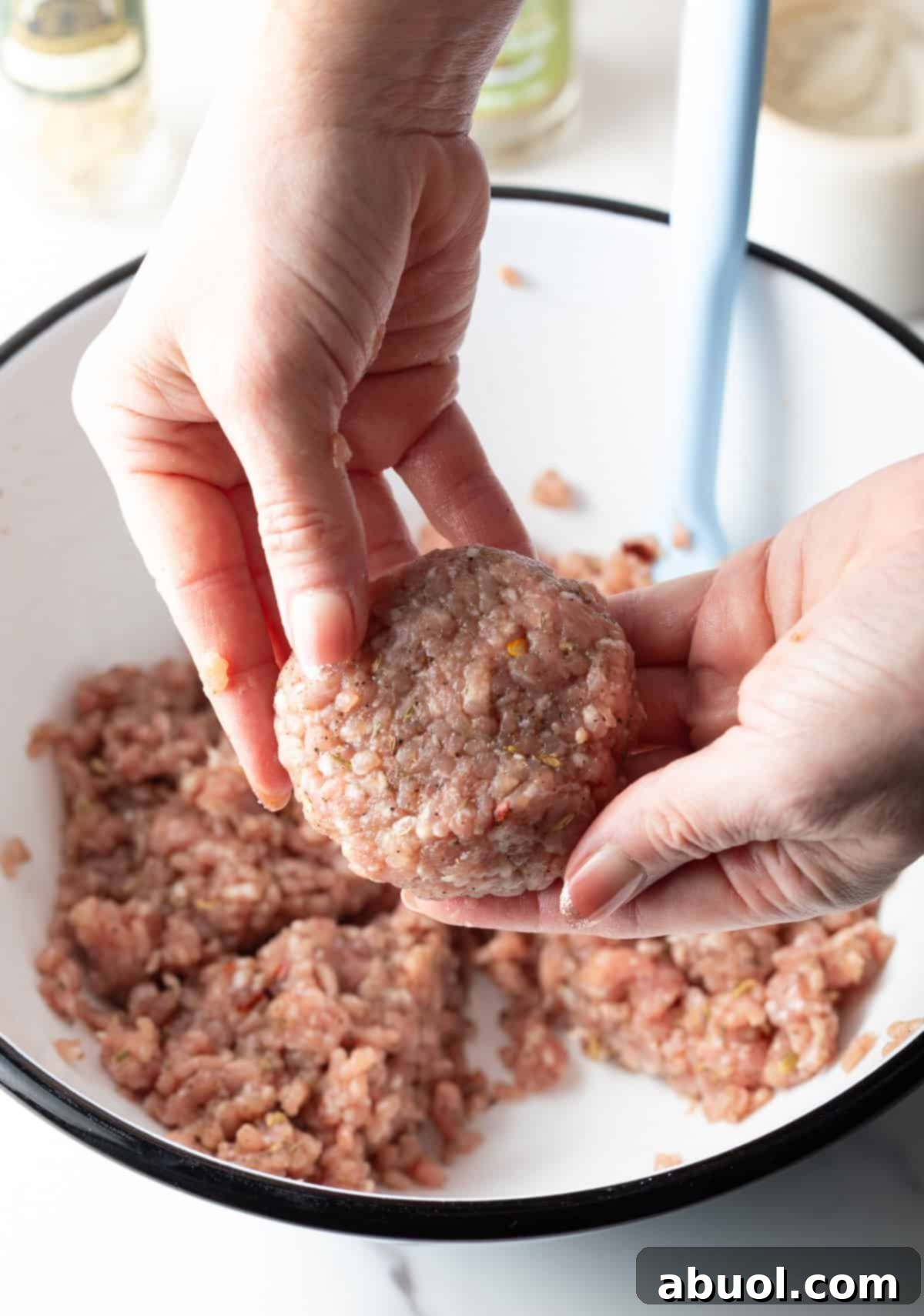 A hand holding a perfectly formed raw breakfast sausage patty above the bowl of sausage mixture.