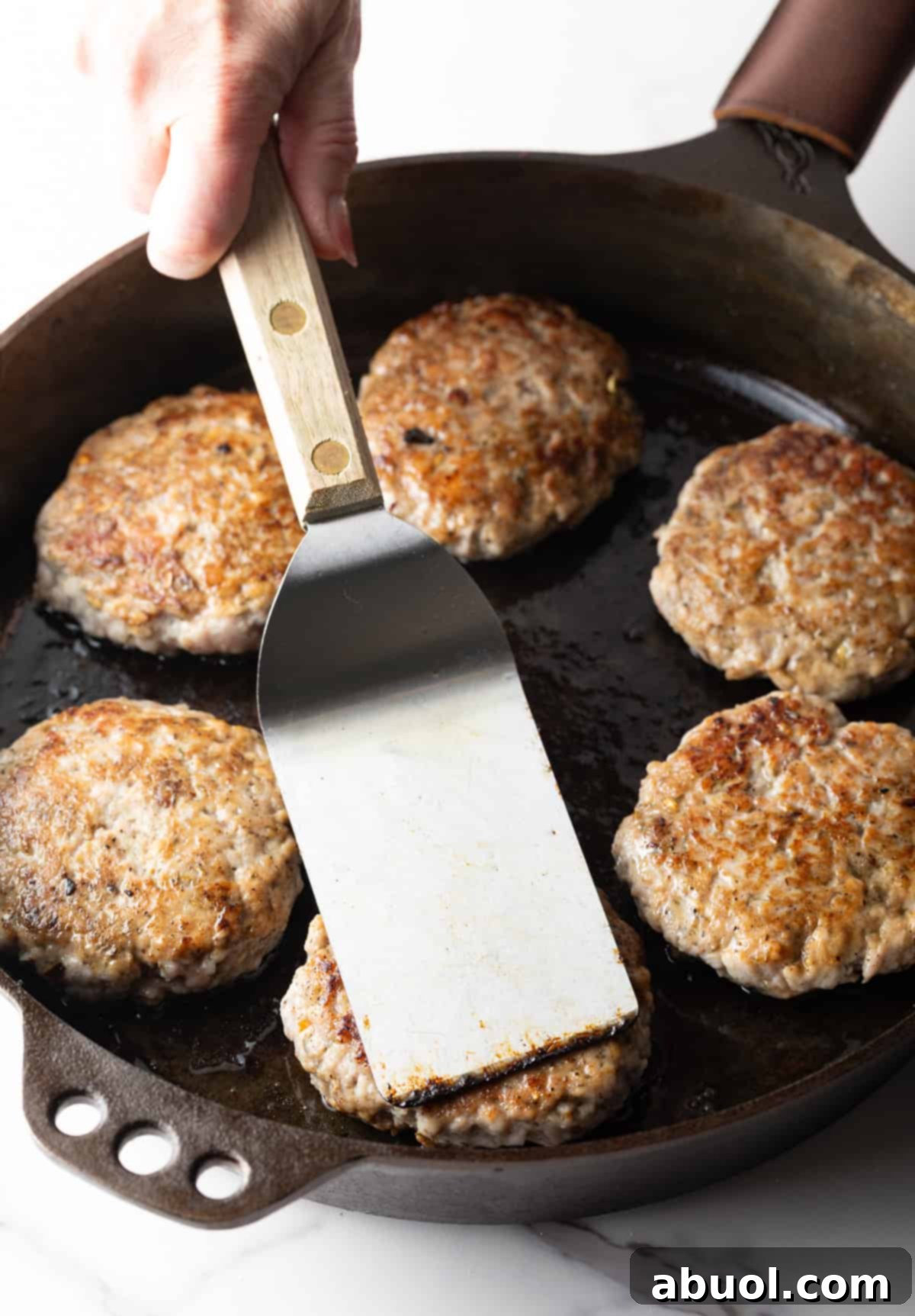 A spatula pressing down on a breakfast sausage patty in a black skillet to ensure an even sear.
