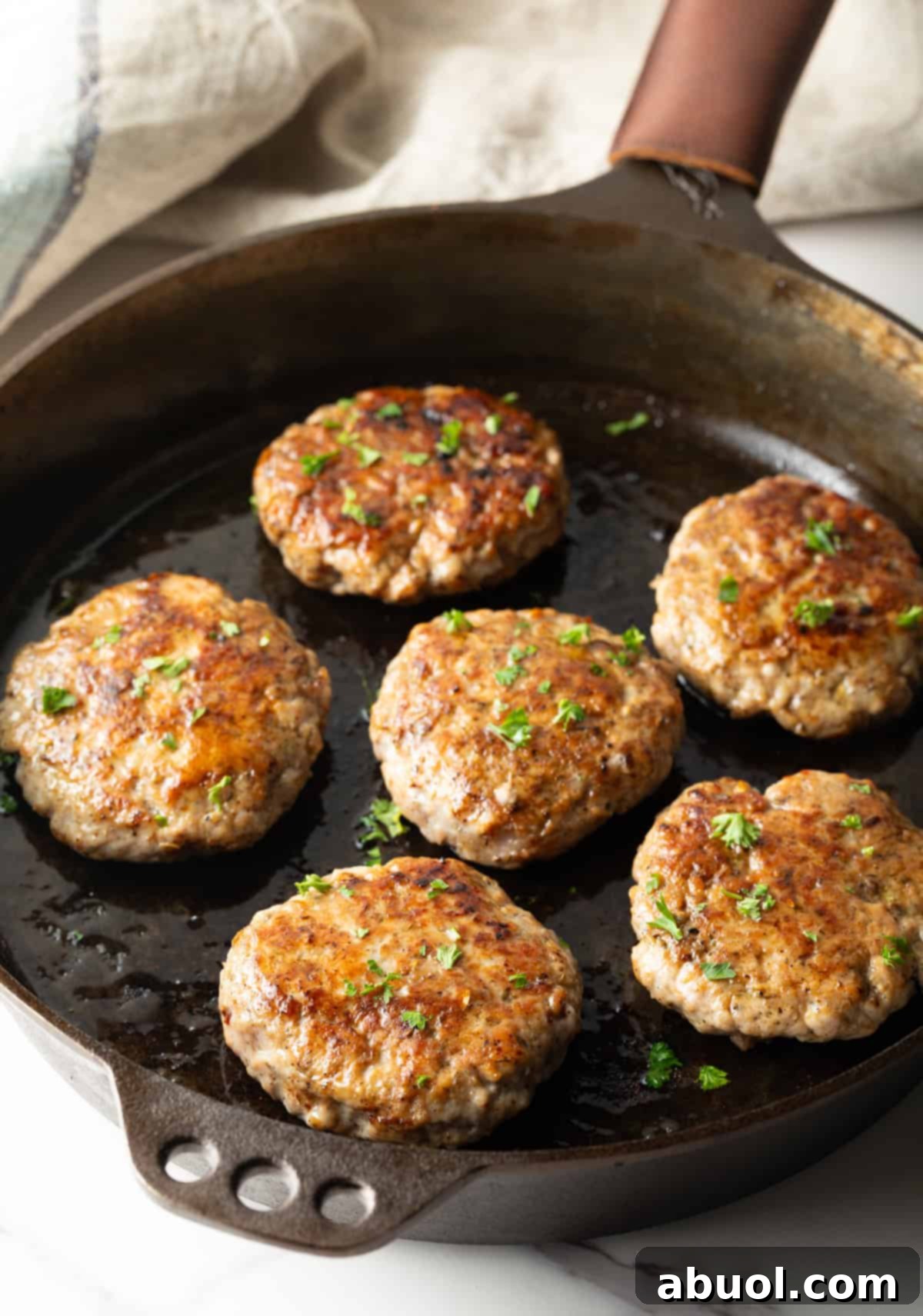 Multiple homemade breakfast sausage patties sizzling and browning in a black skillet.