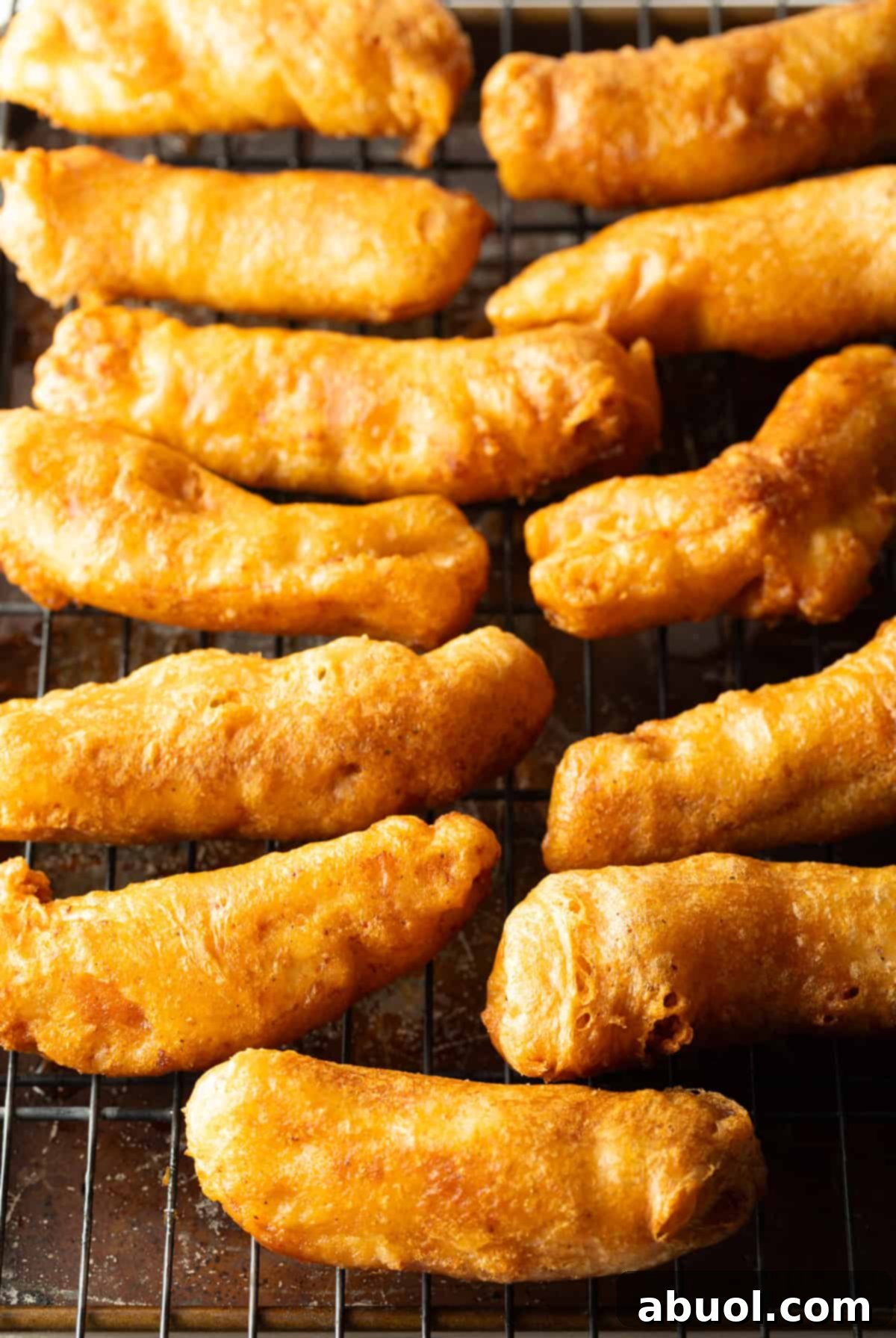 Freshly cooked pieces of beer-battered fish resting on a wire rack to drain and stay crispy.