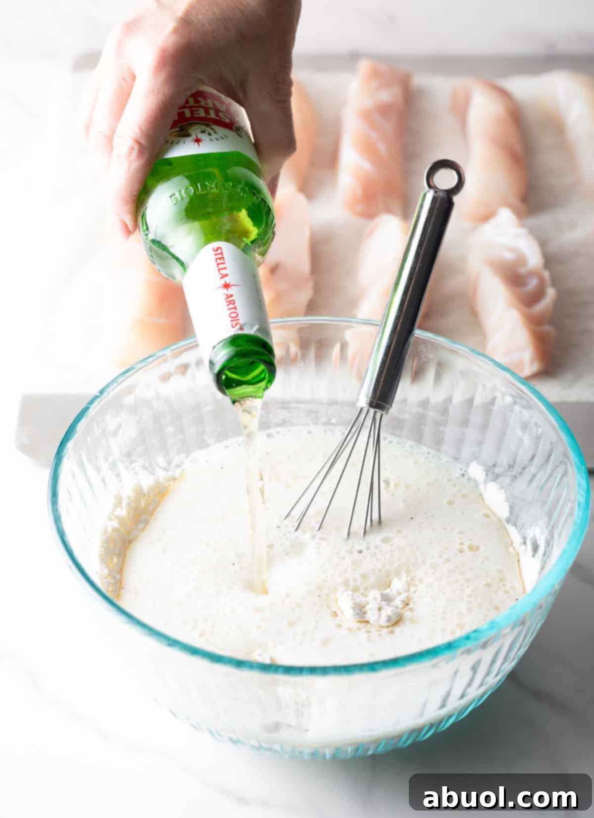 Pouring a light beer into a glass bowl containing the dry ingredients for the fried fish batter.