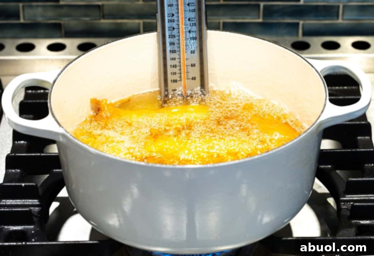 Several pieces of beer-battered fish frying to a golden brown in a pot of hot oil with a thermometer.