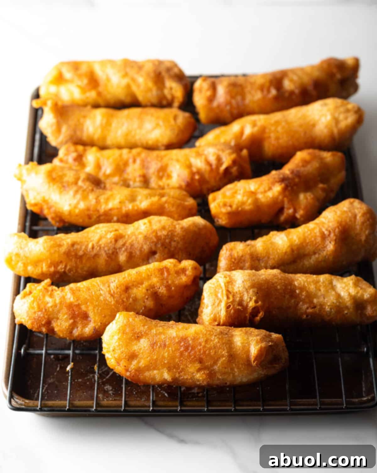 A lineup of perfectly cooked, crispy beer-battered fish fillets cooling on a black wire draining rack.