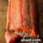 A fillet of cold smoked salmon with a piece flaked off, sitting on a brown surface.