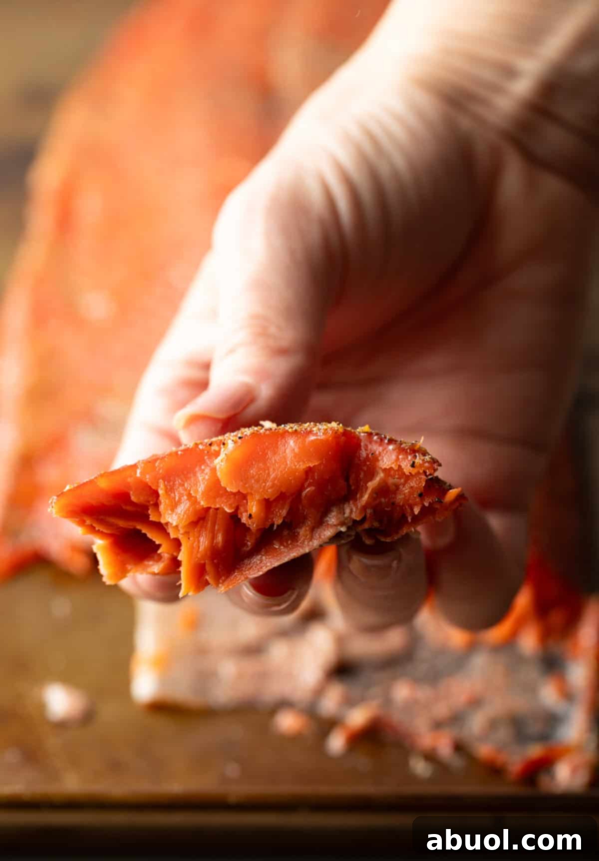 A hand holding a piece of smoked salmon, showcasing its flaky texture.