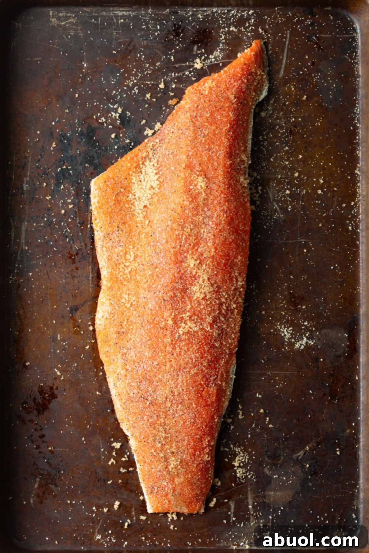 A raw salmon fillet on a baking sheet, seasoned with brown sugar and spices, ready for the smoker.
