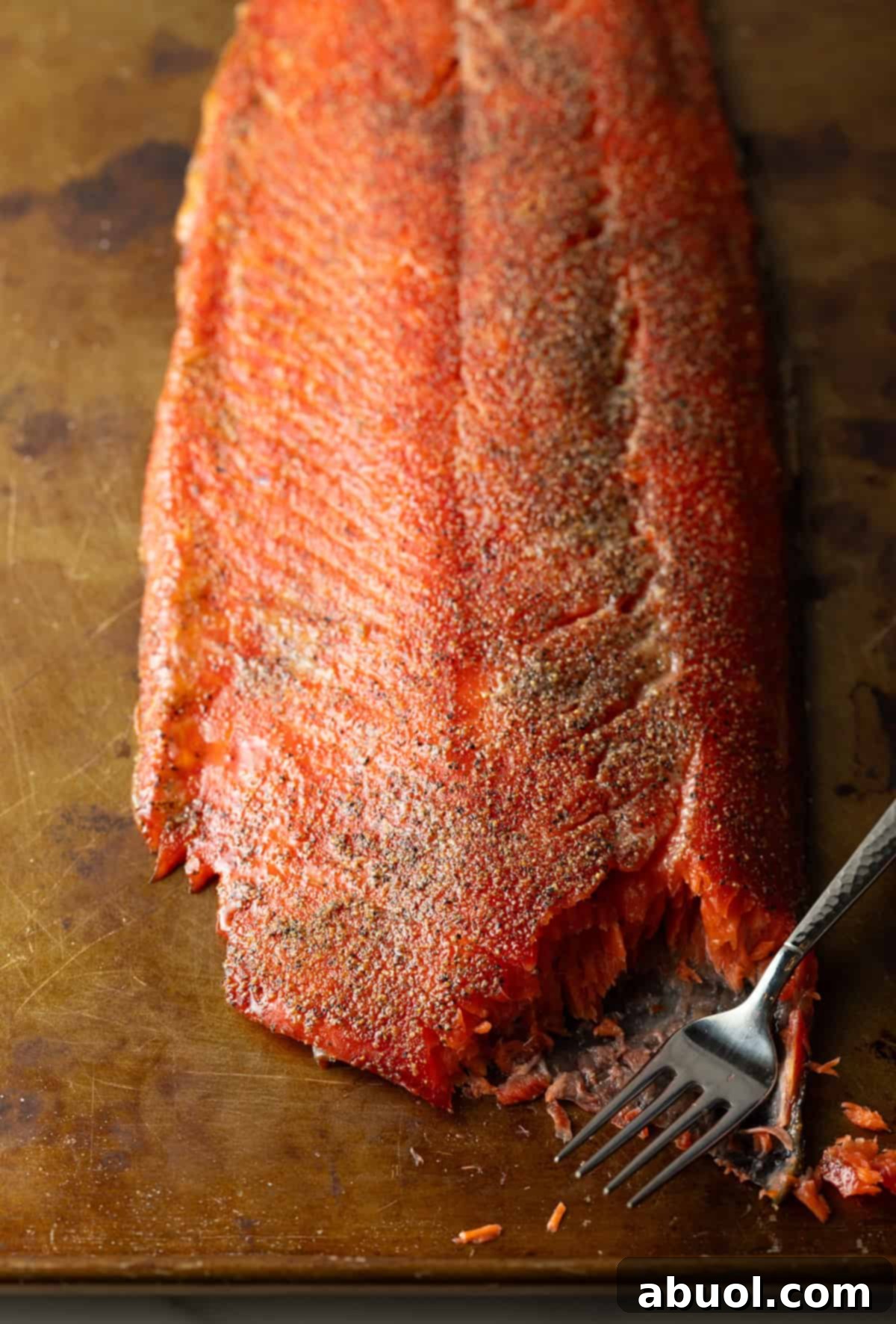 A fork flaking a piece from a whole cold smoked salmon fillet to show the moist interior.