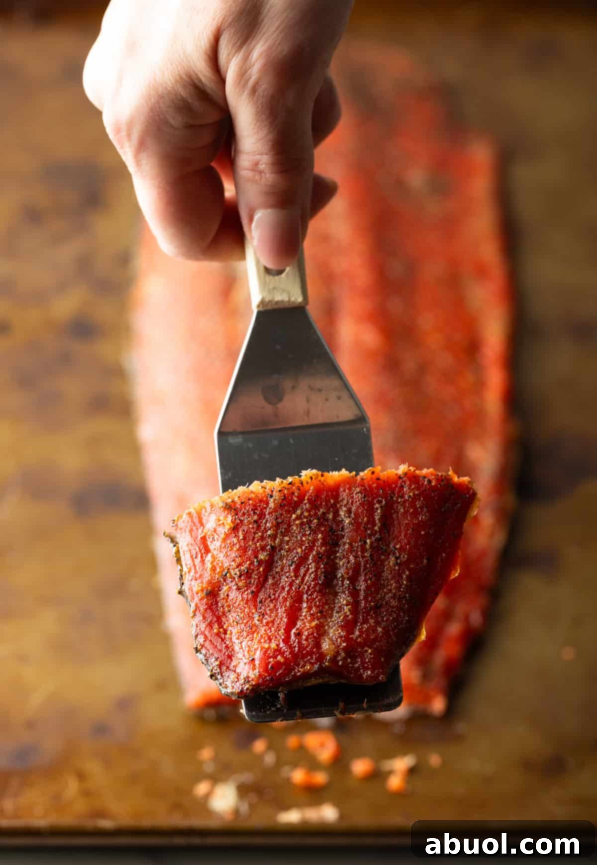 A metal spatula lifting a perfectly cooked slice of cold smoked salmon.