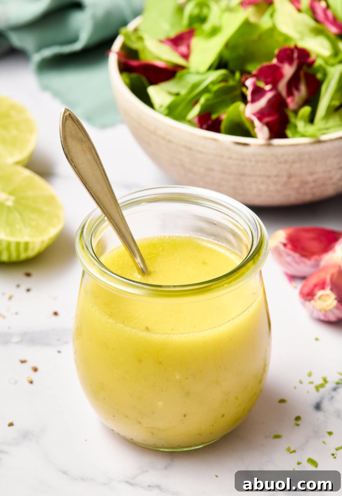 Creamy honey lime vinaigrette in a clear glass jar with a small serving spoon.