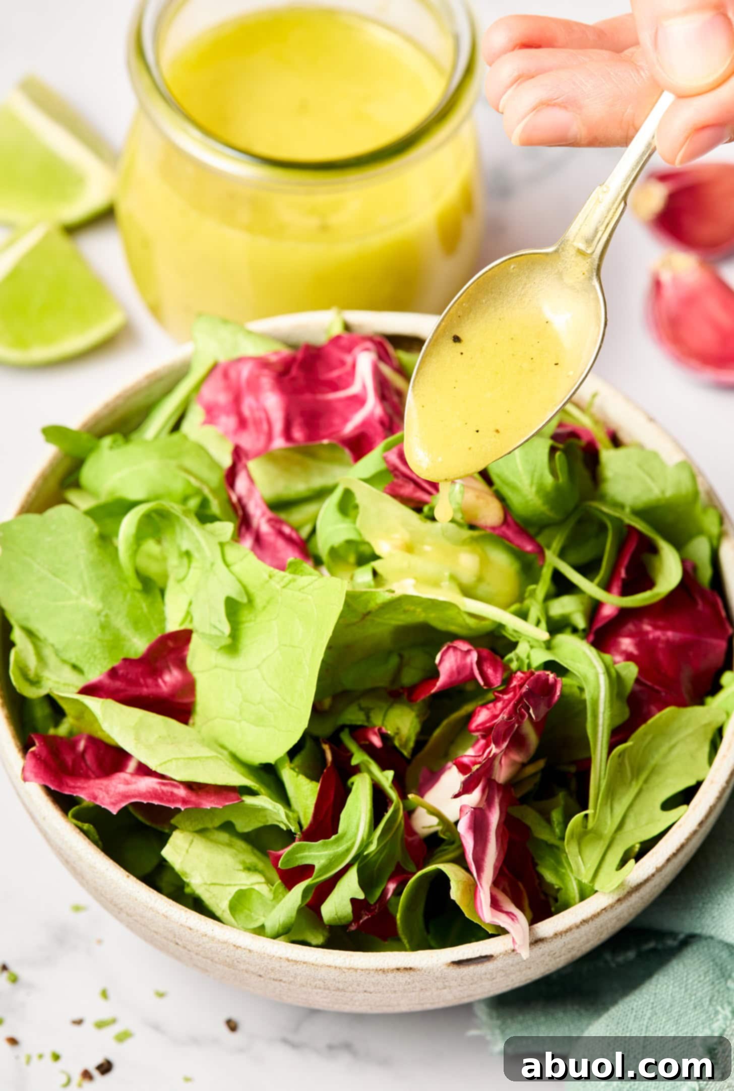 A spoonful of creamy lime vinaigrette being drizzled over a bed of fresh salad greens.