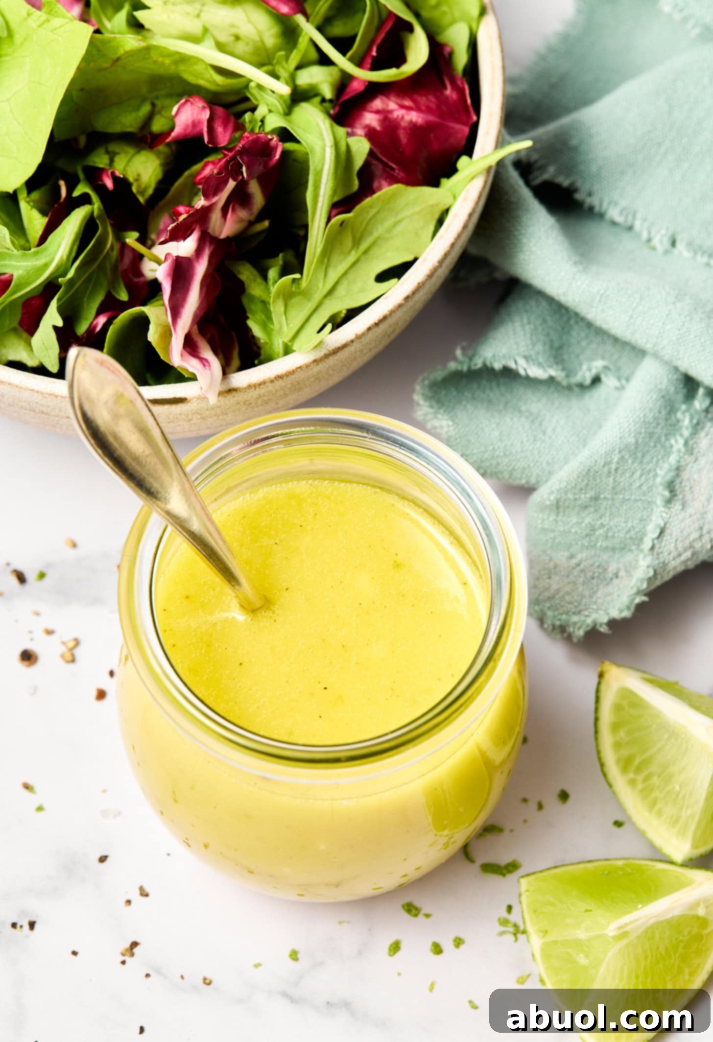 An overhead view of the finished lime vinaigrette in a jar, surrounded by fresh limes and a salad.