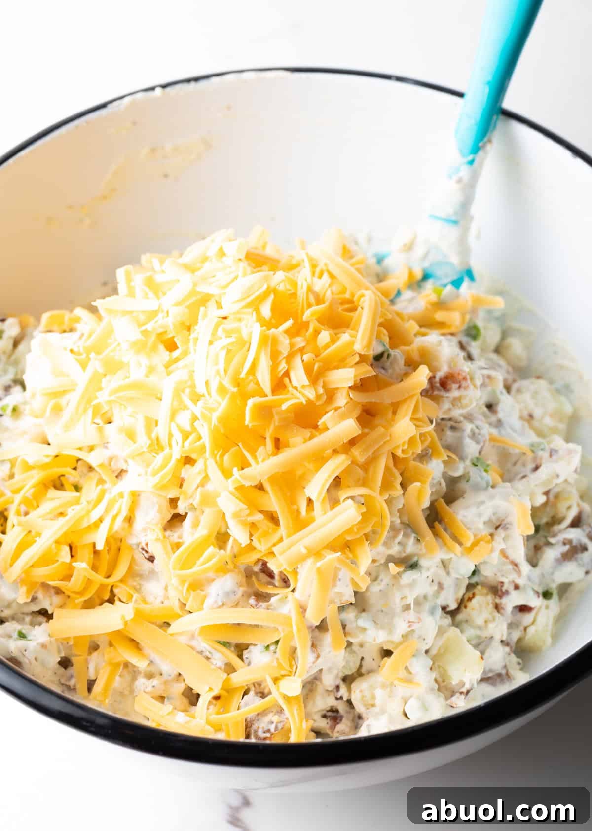A bowl filled with loaded baked potato salad, topped with shredded cheddar cheese.