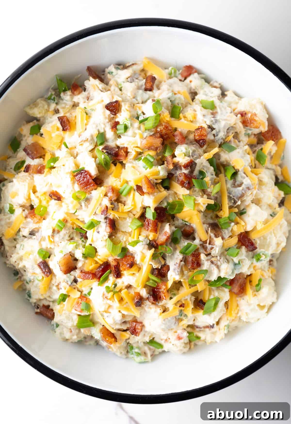 An overhead shot of a loaded baked potato salad recipe in a white bowl.
