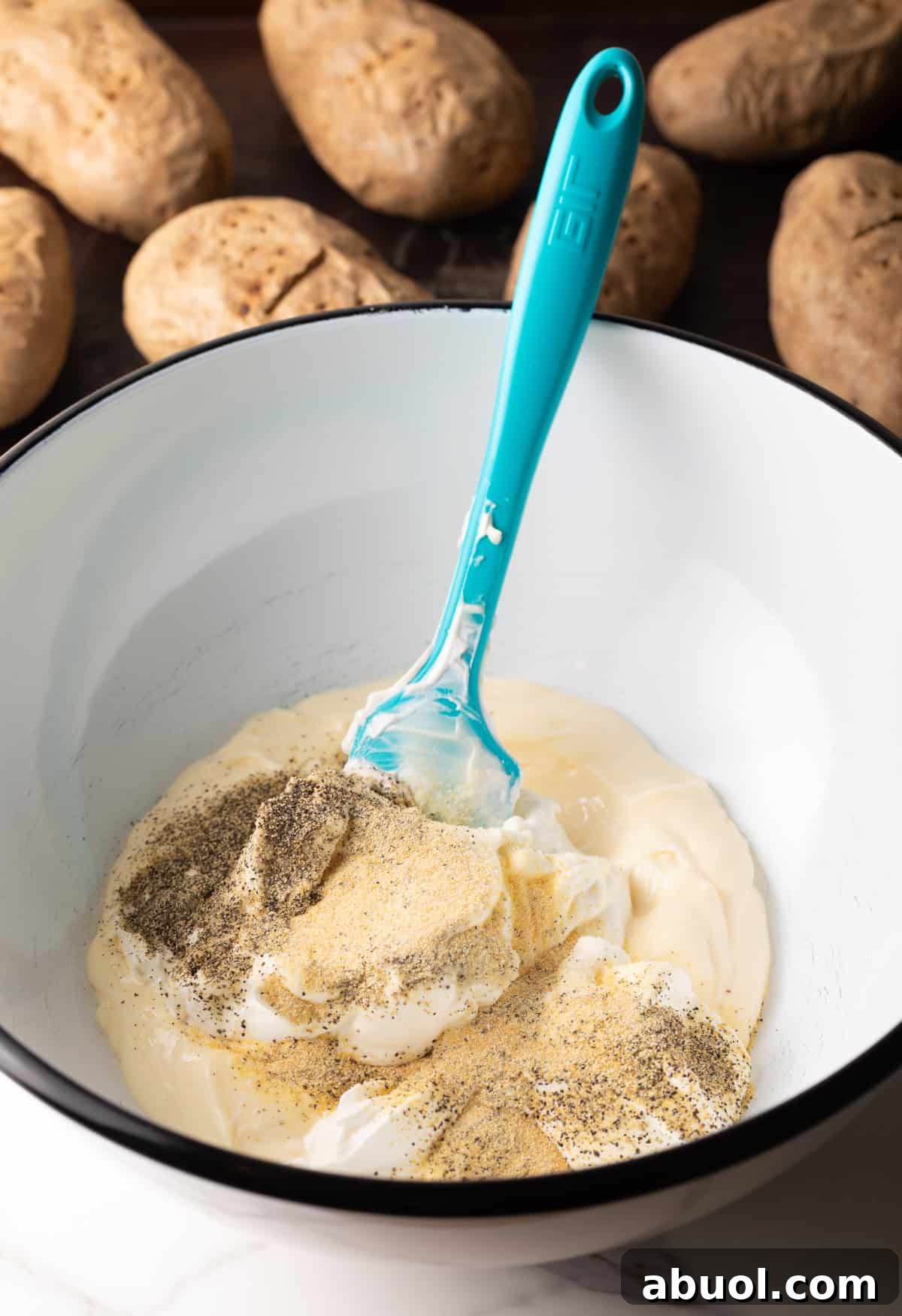 Ingredients for the dressing for a baked potato salad recipe are being stirred in a white bowl.
