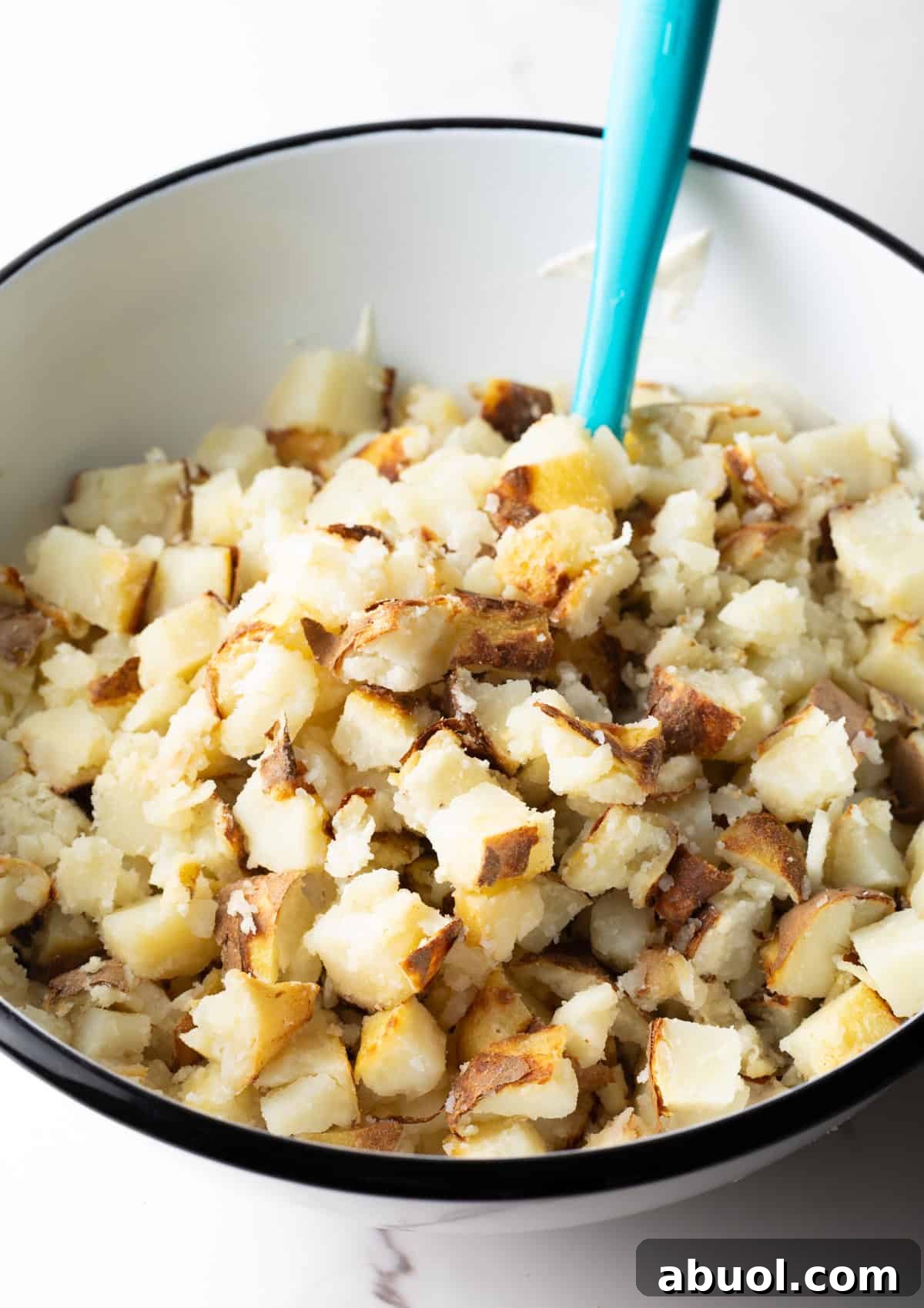 Baked potato chunks sitting in a bowl with a blue spatula.