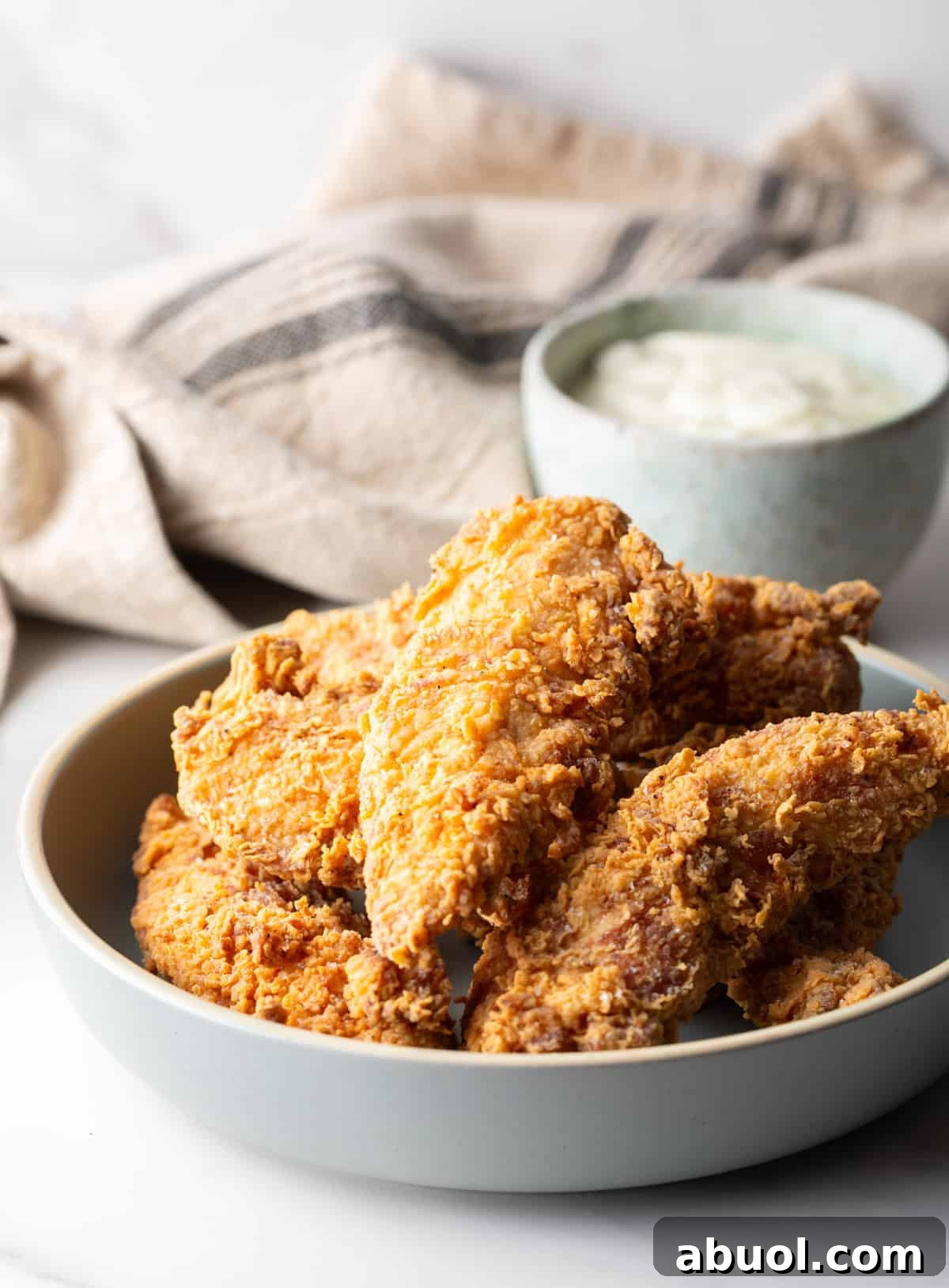 A white bowl filled with deep fried chicken tenders, with a ramekin of white sauce on the side.