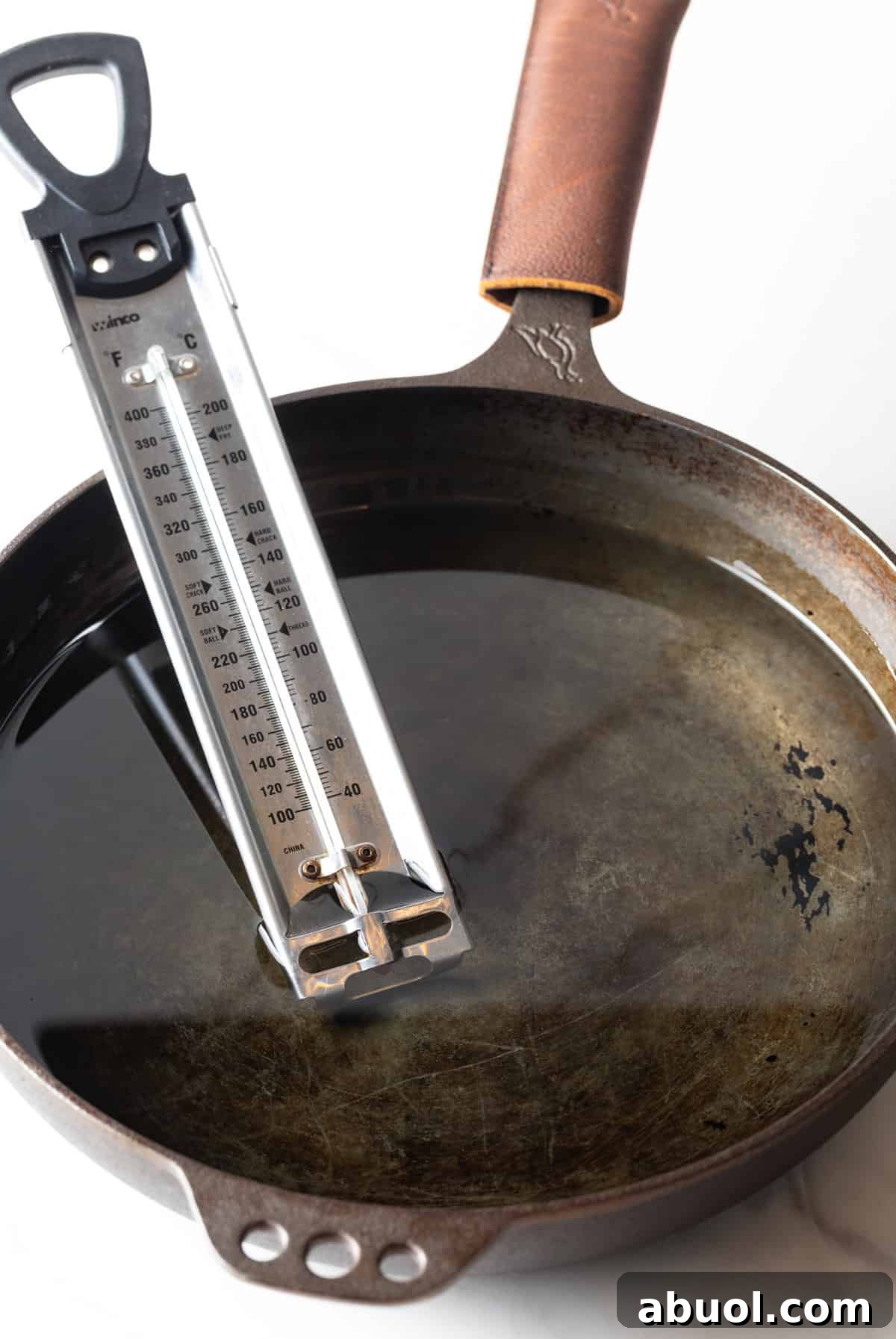 A cooking thermometer is being used in a black skillet filled with cooking oil.