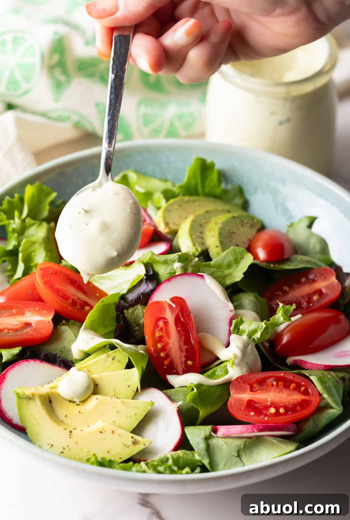 Creamy Avocado Lime Ranch Dressing Recipe 11 A spoon is drizzling homemade Chick Fil A avocado lime ranch dressing over a salad with tomatoes and avocados.
