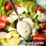 Creamy Avocado Lime Ranch Dressing Recipe 12 A spoon is drizzling homemade avocado lime ranch dressing over a salad with tomatoes and avocados.