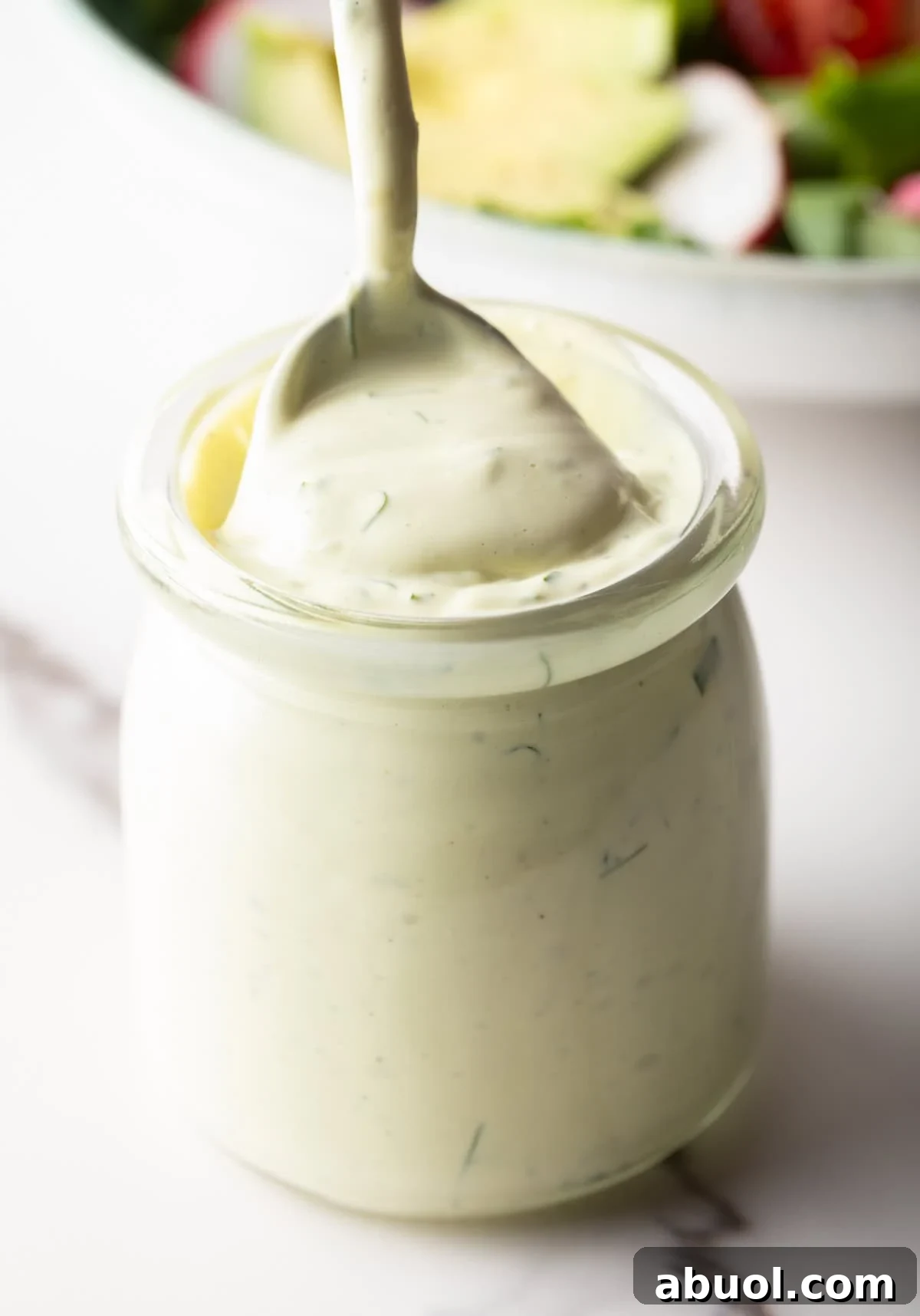 Creamy Avocado Lime Ranch Dressing Recipe 10 A jar filled with creamy avocado lime ranch dressing, with a spoon scooping a serving.