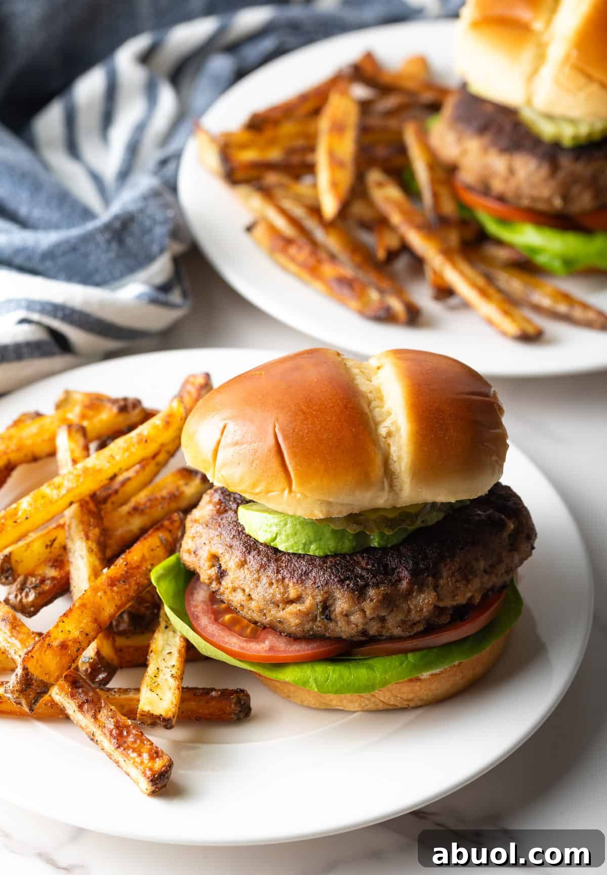 A thick and juicy ground turkey burger sitting on a white plate next to French fries.