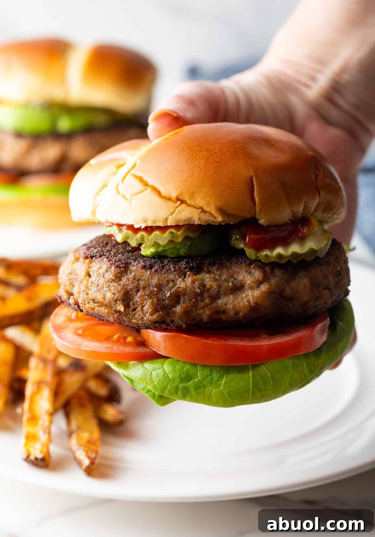 A hand holding a thick ground turkey burger with pickles, lettuce, and tomato.
