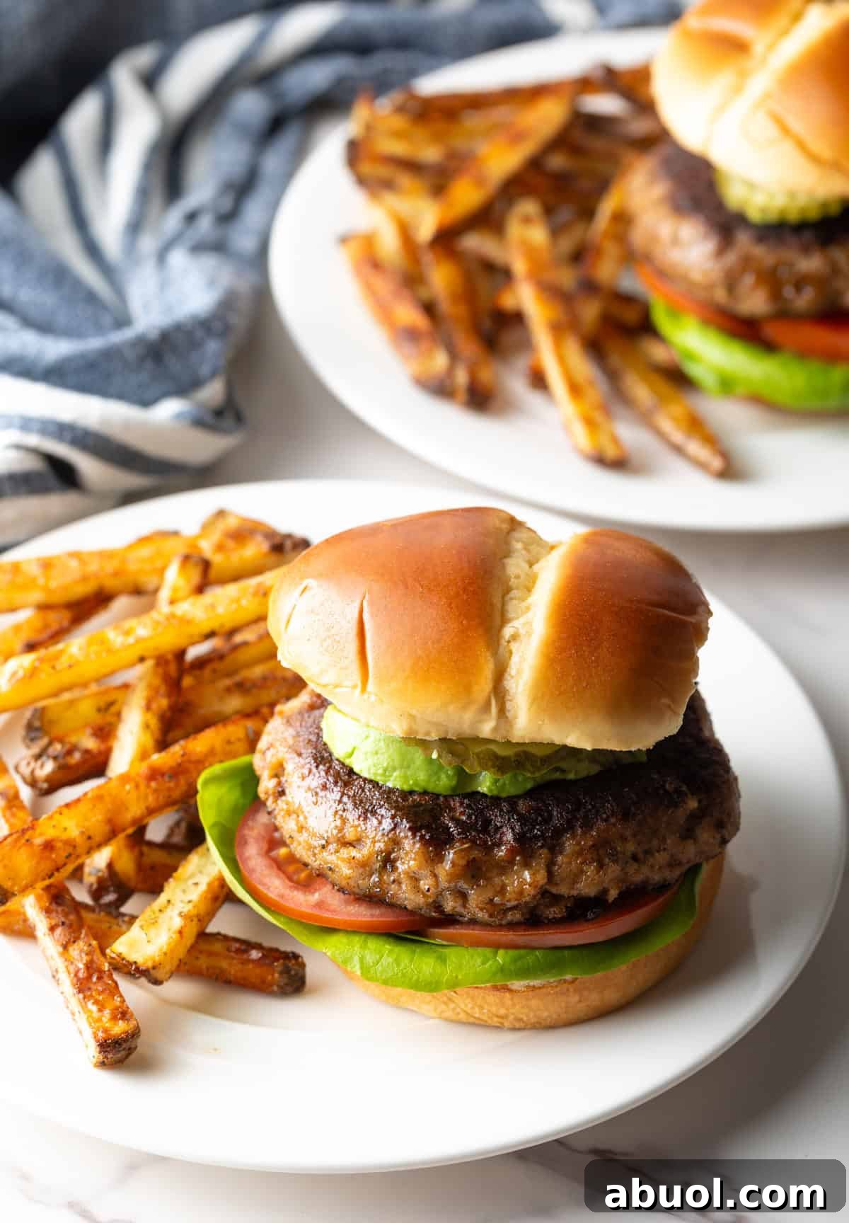 A homemade ground turkey burger inside of a hamburger bun, sitting on a white plate with fries.
