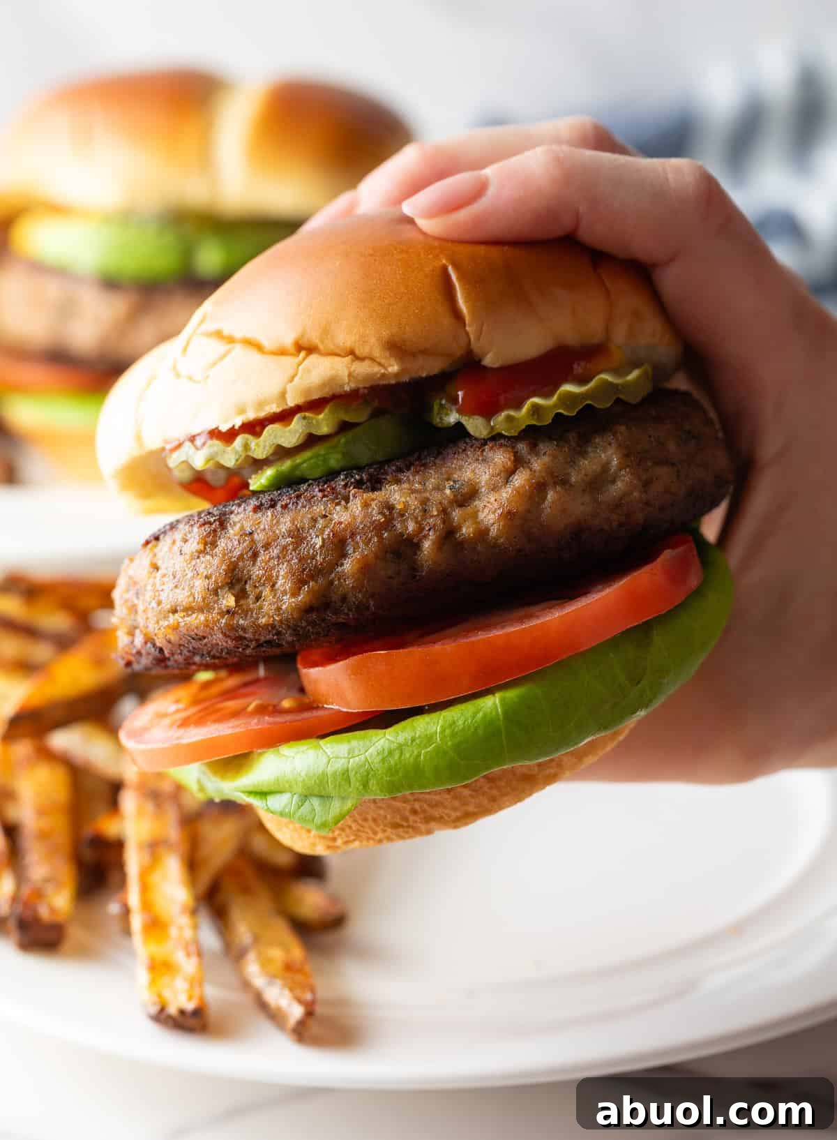 A hand holding a thick turkey burger with pickles, lettuce, and tomato.