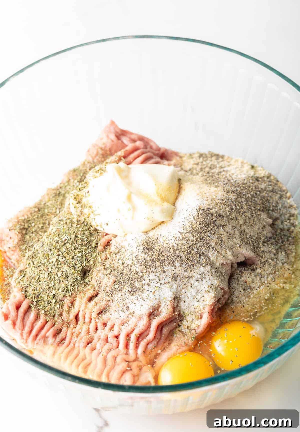 A glass bowl filled with ground turkey, eggs, and seasonings for a turkey burger recipe.