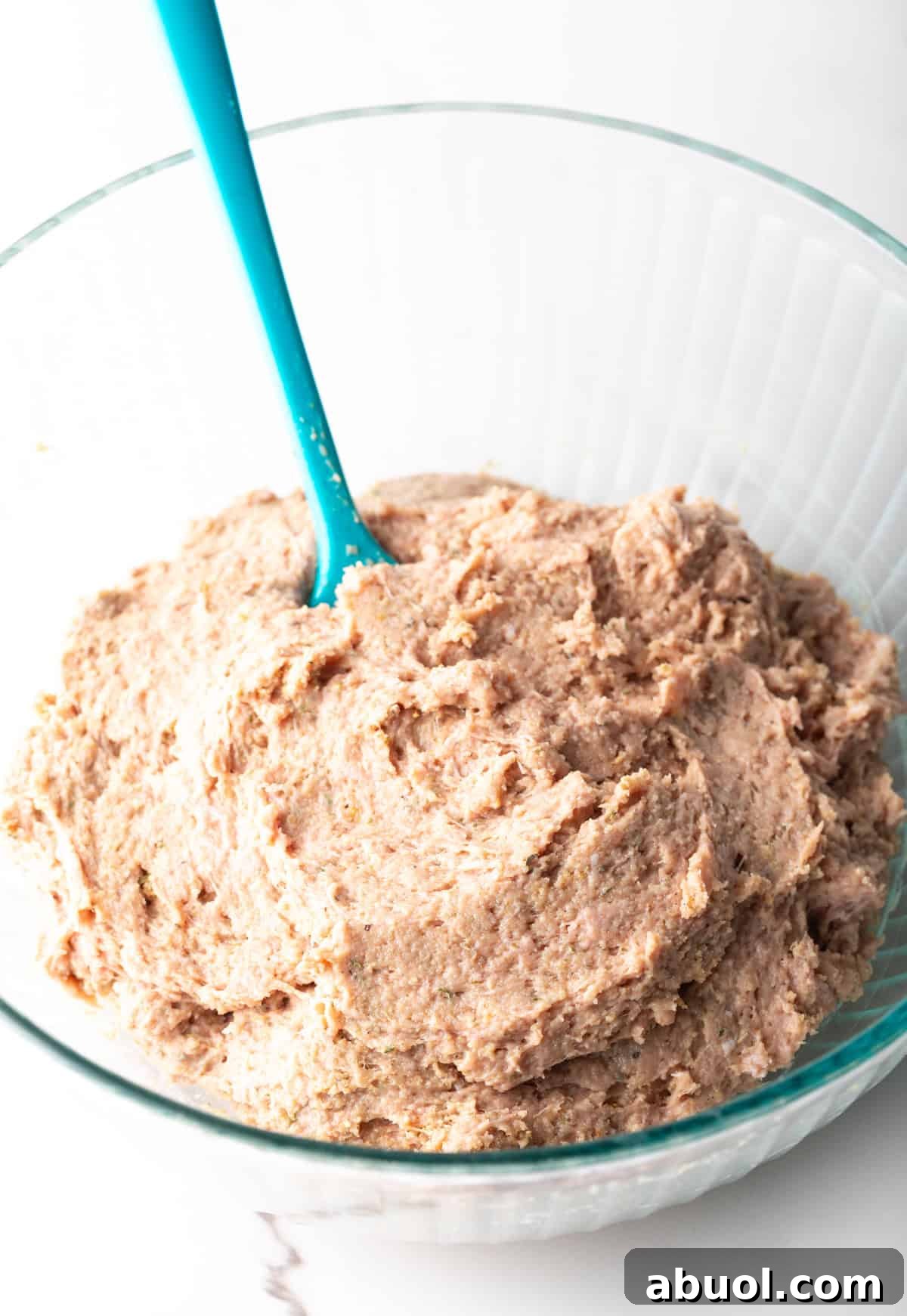 A ground turkey burger mixture in a glass bowl with a blue spatula.