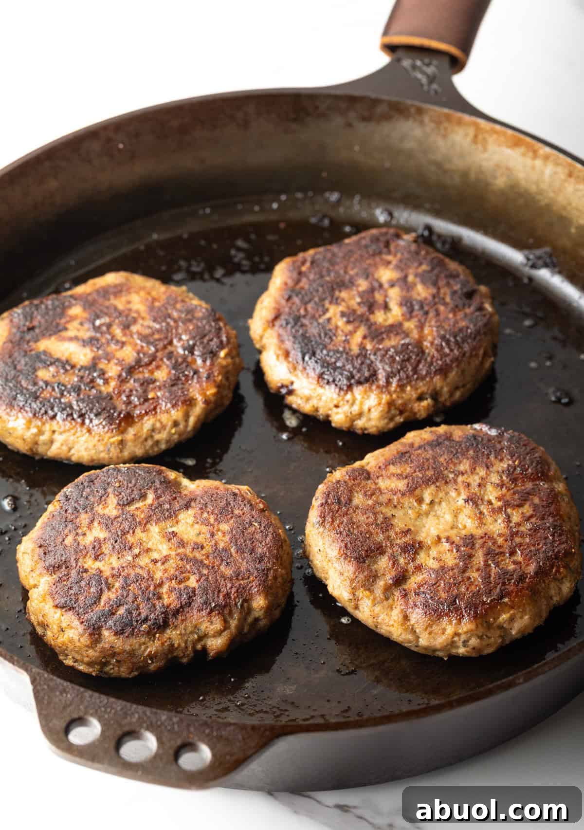 Homemade ground turkey burger patties are being cooked in a black skillet.