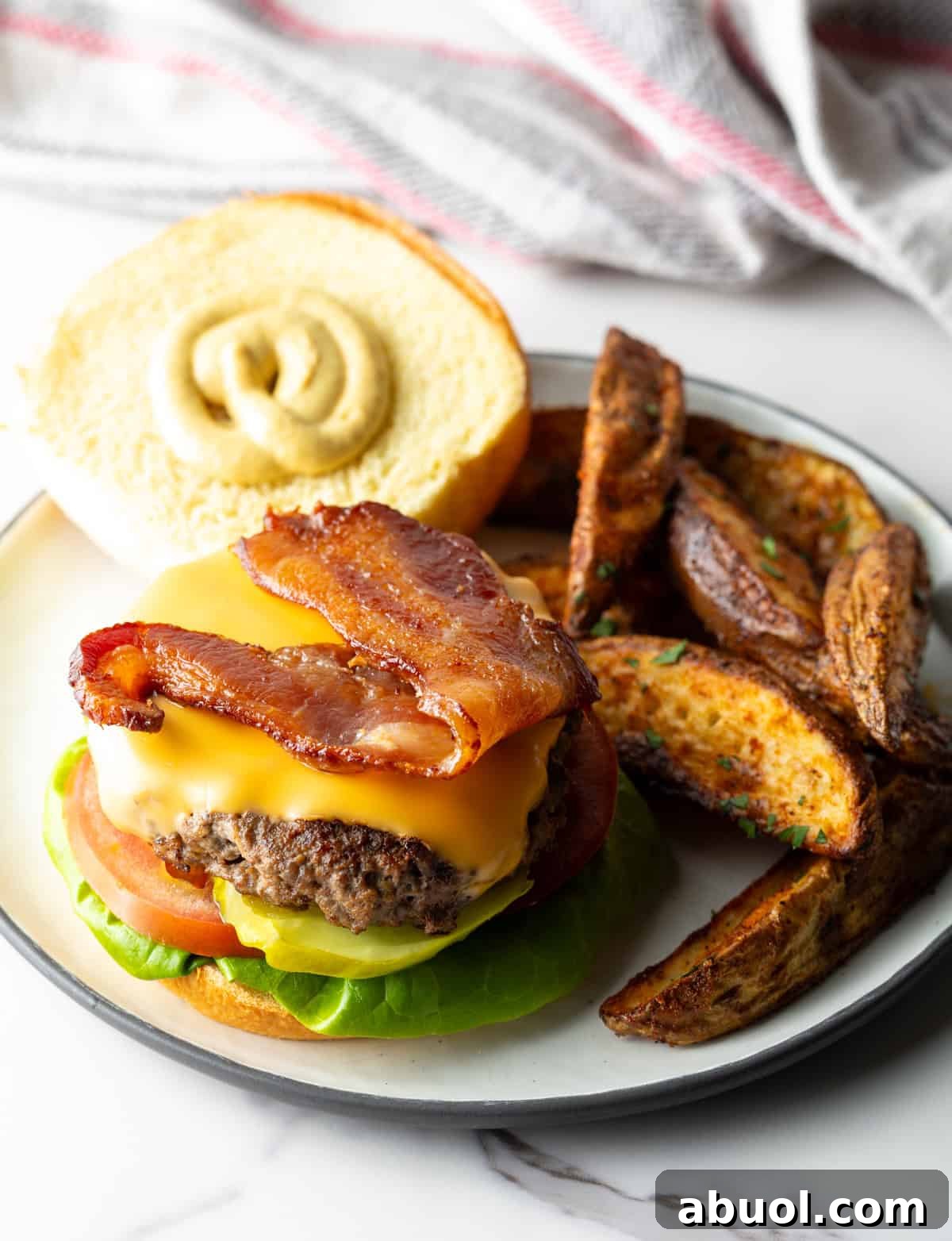 An deer hamburger with the top bun off, showing it is topped with cheese and bacon.