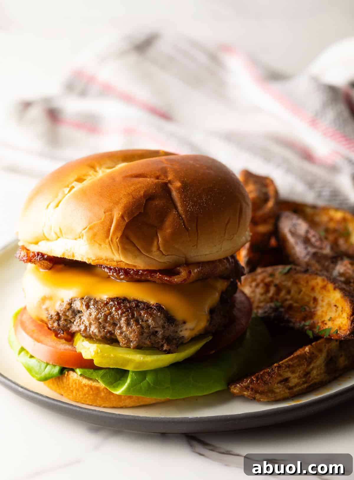 A deer burger recipe topped with melted cheese, sitting on a plate with potato wedges.