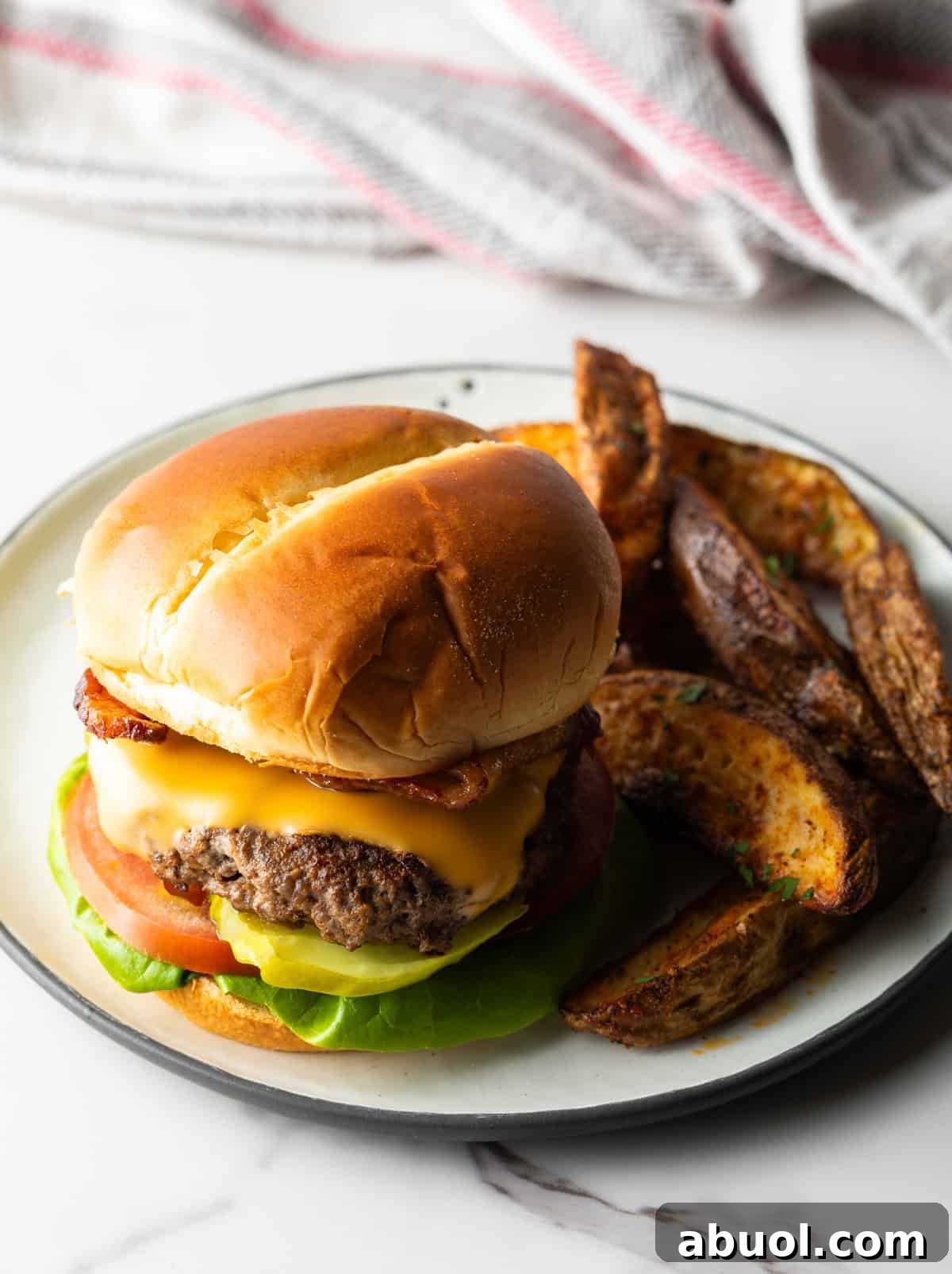 A deer hamburger recipe topped with melted cheese, sitting on a plate with potato wedges.