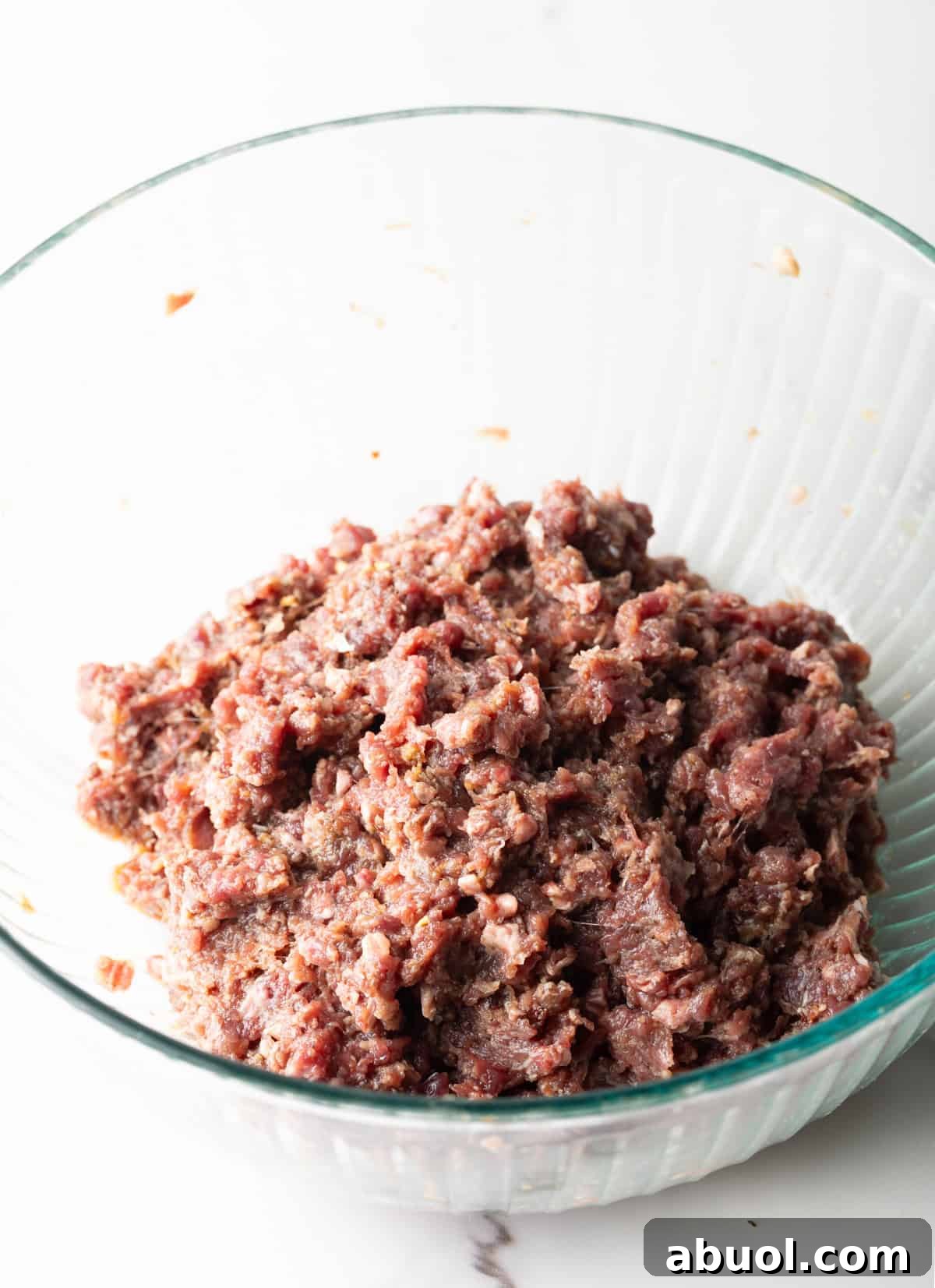 A meat mixture for a deer hamburger recipe is in a glass bowl.