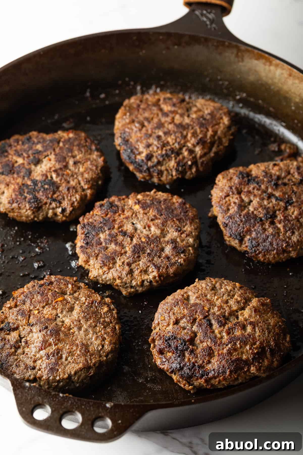 Deer burger patties are being grilled in a black skillet.