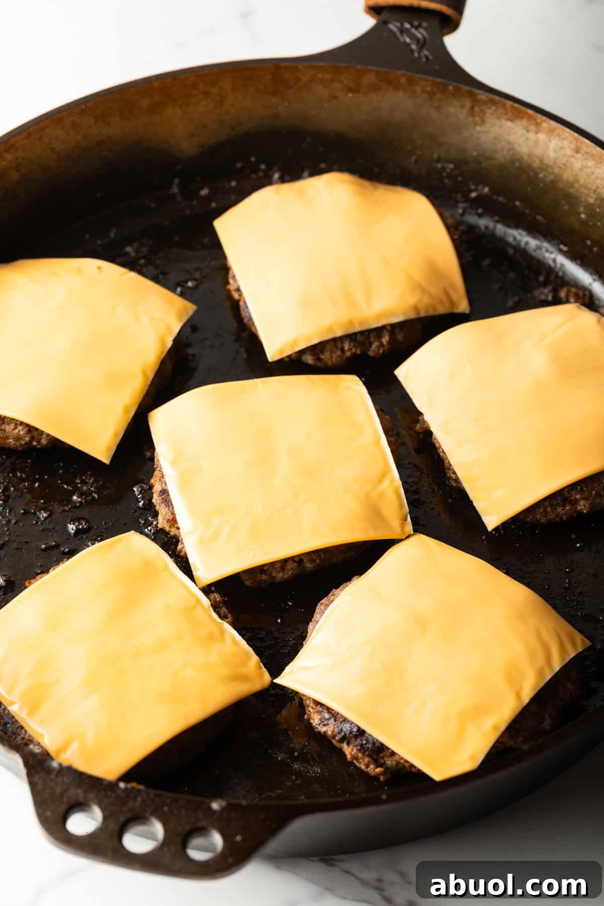 Venison burger patties topped with cheese in a black skillet.