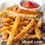 Homemade oven baked French fries sitting on a white plate with a ramekin of ketchup.