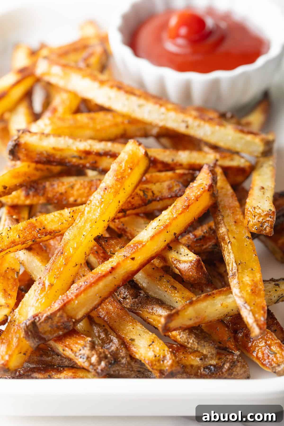 Homemade French fries made in the oven, sitting on a white plate next to a ramekin of ketchup.