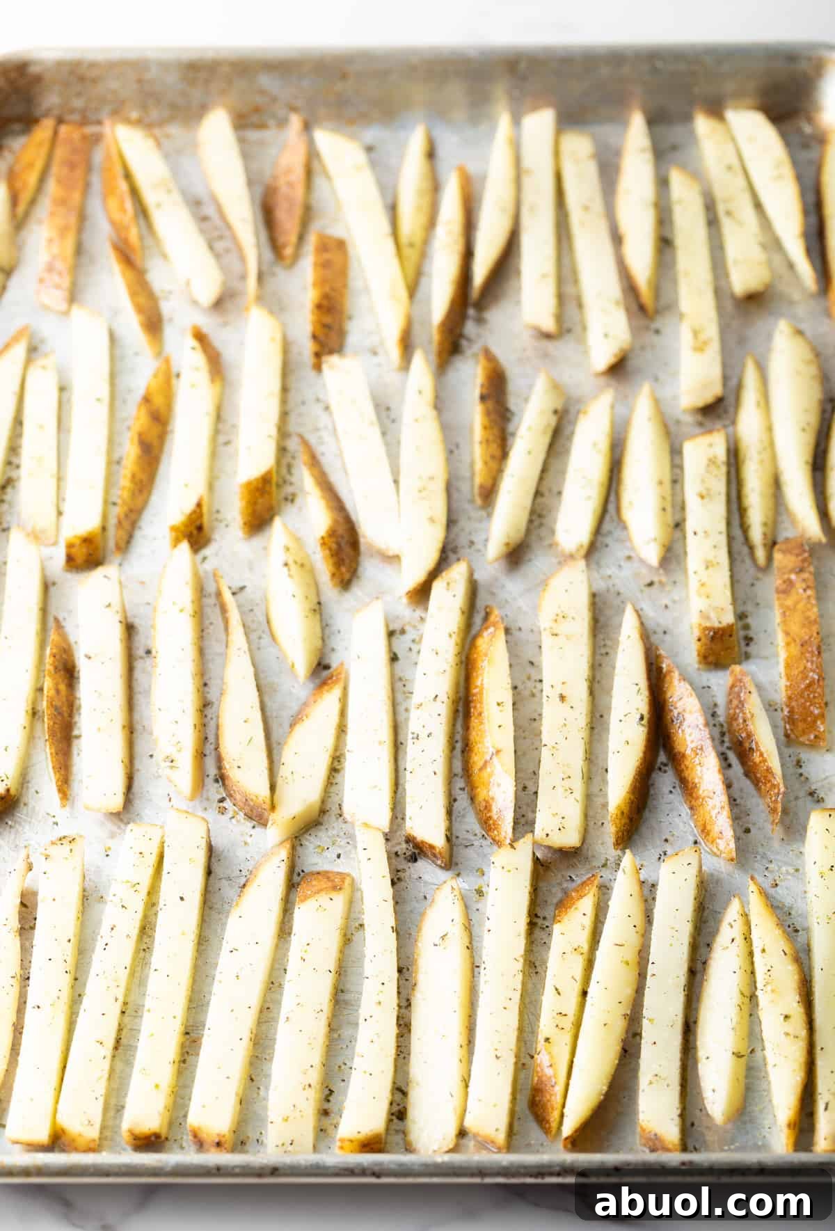 Raw homemade French fries arranged on a baking sheet, ready to be baked in the oven.