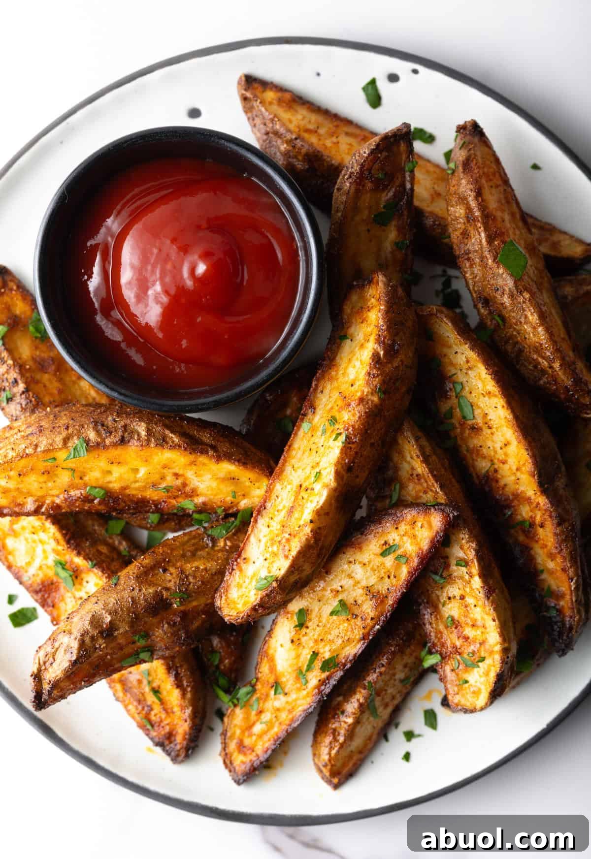 A plate of crispy oven baked potato wedges with a ramekin full of ketchup.
