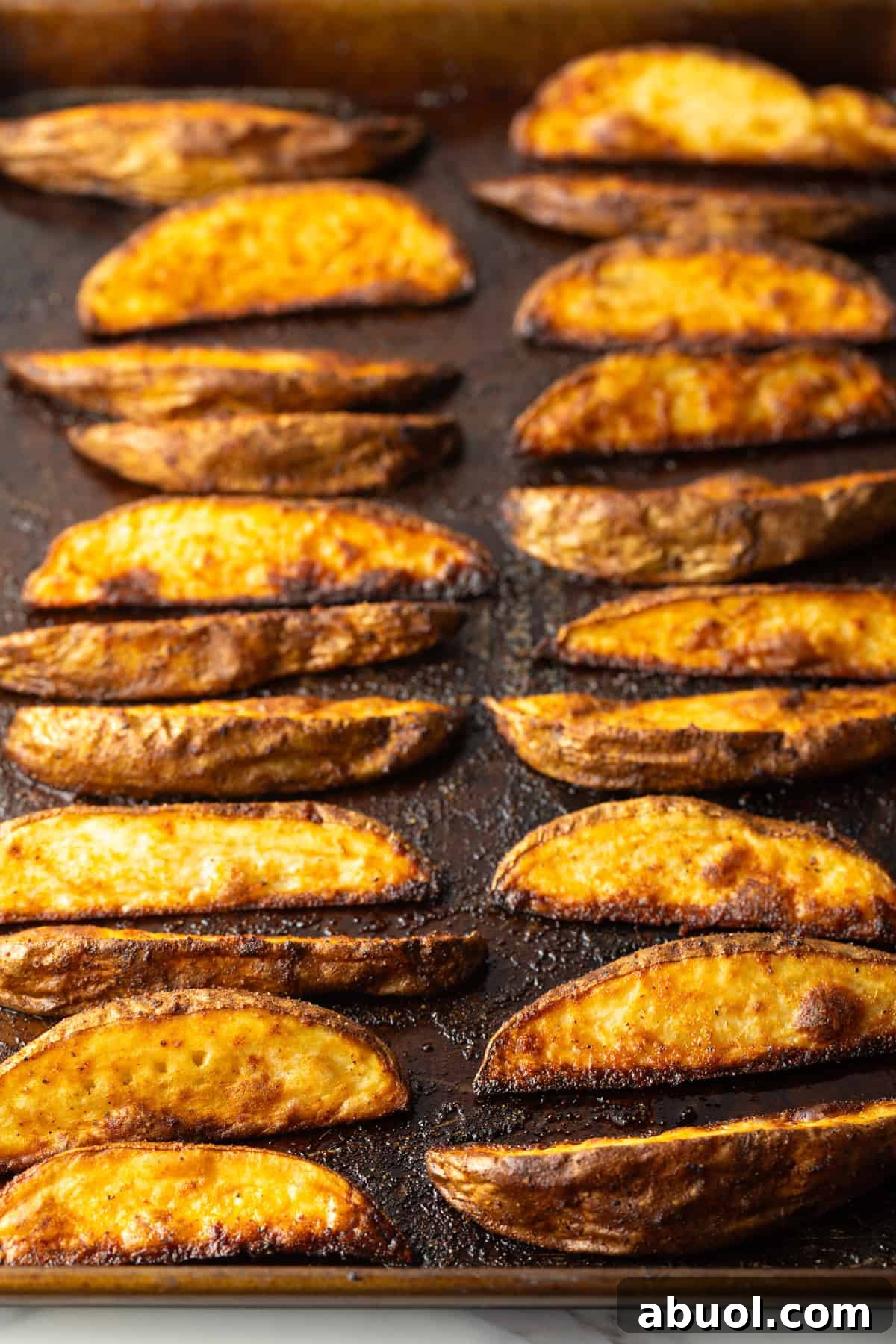 Freshly baked oven baked potato wedges on a black baking sheet.
