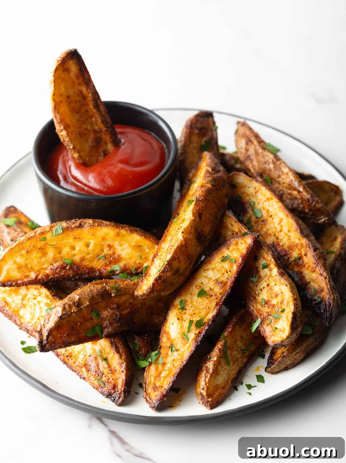 A plate of oven baked potato wedges, one of the wedges is in a ramekin of ketchup.
